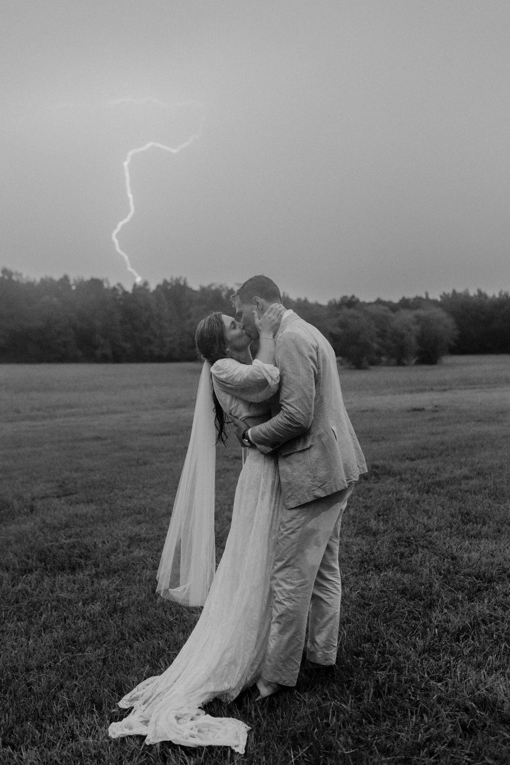 The bride and groom kiss in the rain as lightning strikes on the Southern wedding day.