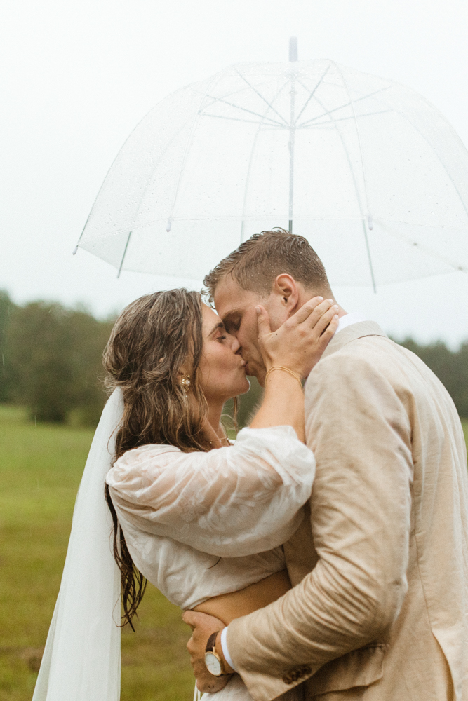 The bride and groom kiss under an umbrella on a rainy wedding day in Alabama.