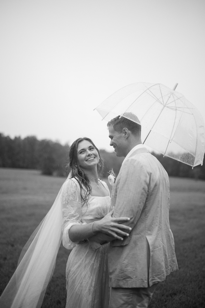 The bride and groom embrace under an umbrella on a rainy wedding day in Alabama.