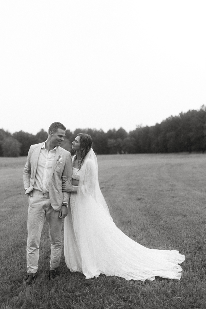 The bride holds the groom's arm in an Alabama field.