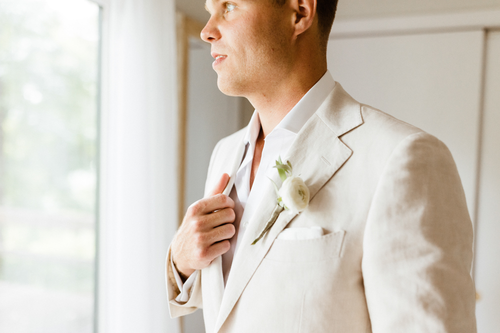 The groom holds his suit jacket as he looks out the window.