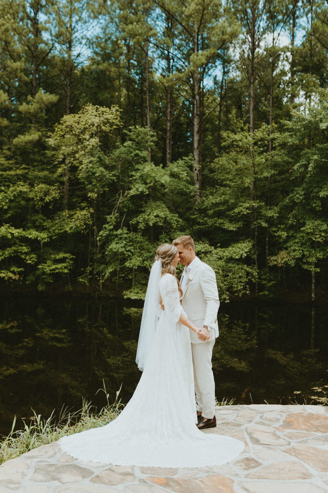 The bride and groom smile together as they stand by the creek.