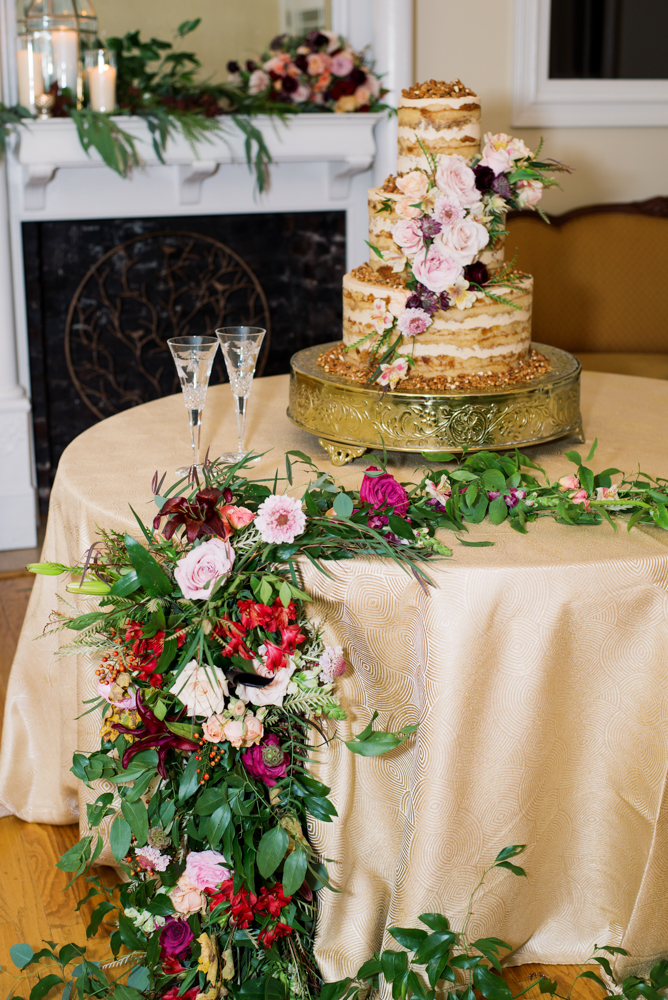 The wedding cake by Daughter's Baking is decorated with a floral garland for this Birmingham wedding.