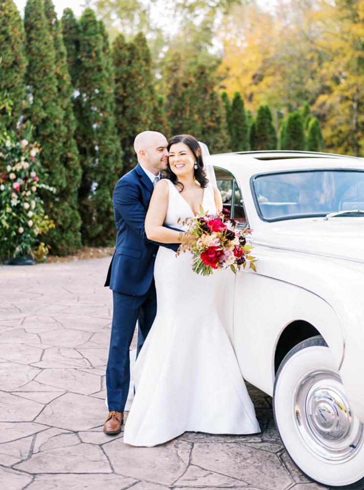 The bride and groom embrace next to their getaway car after their Birmingham, Alabama wedding.