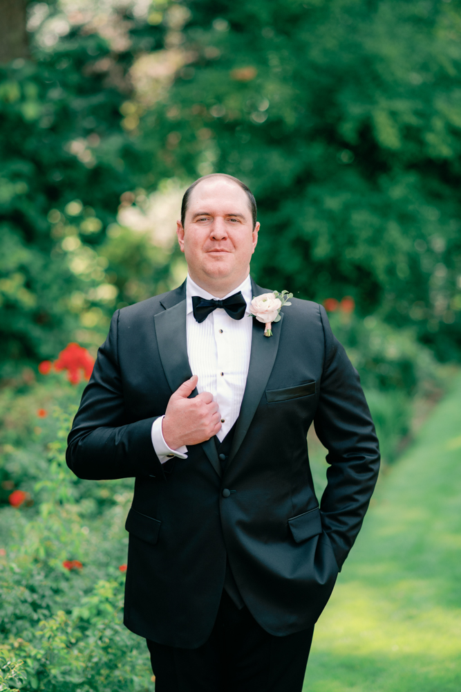 The groom holds the lapel of his tuxedo at Birmingham Botanical Gardens.