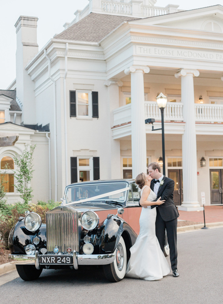 The bride and groom kiss next to their car from Coats Classic Cars outside of Huntsville Botanical Garden.