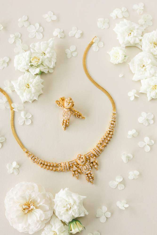 The wedding jewelry is styled in a lay flat with white flowers.