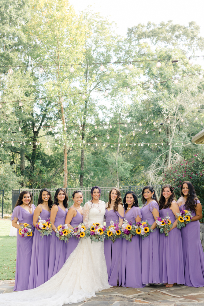 The bride stands with her bridesmaids in purple bridesmaid dresses with bouquets of sunflowers at Mathews Manor.