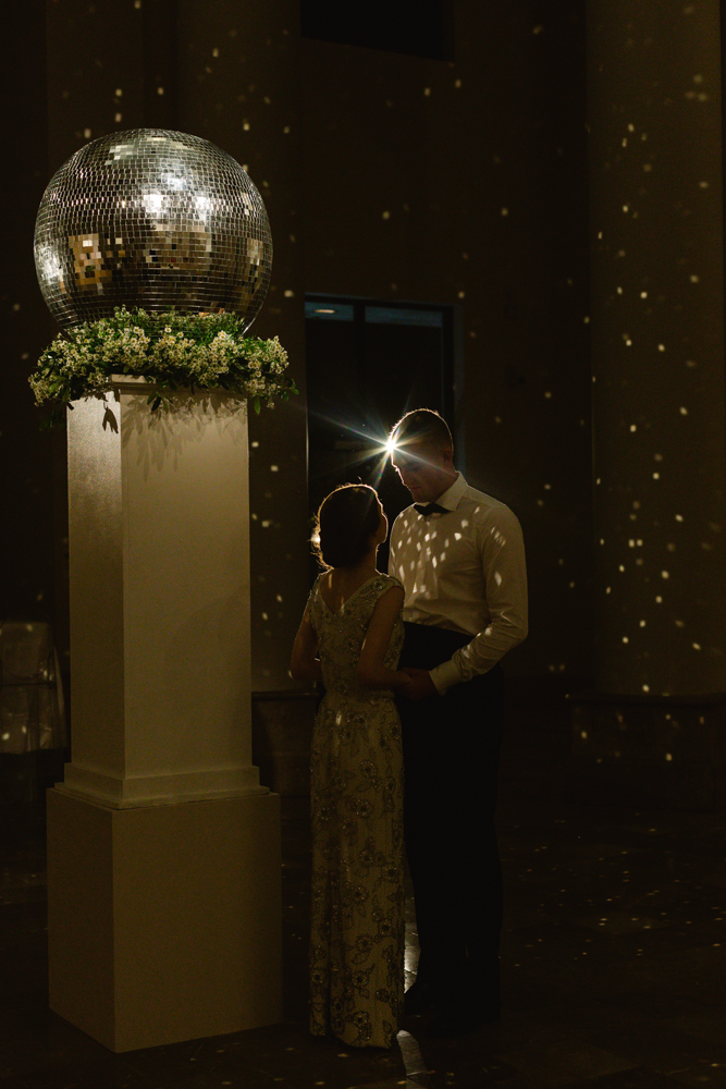 The bride and groom stand beneath a disco ball at the Southern wedding reception.