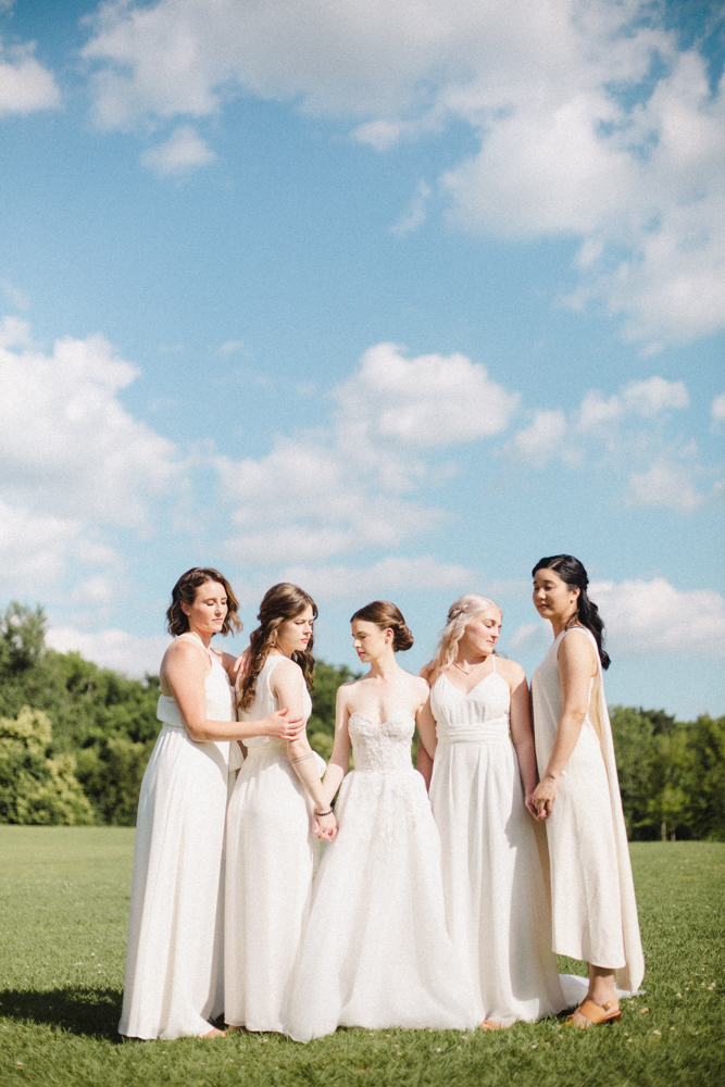 The bride stands with her bridesmaids wearing ivory bridesmaid dresses in the field outside Montgomery Museum of Fine Arts.