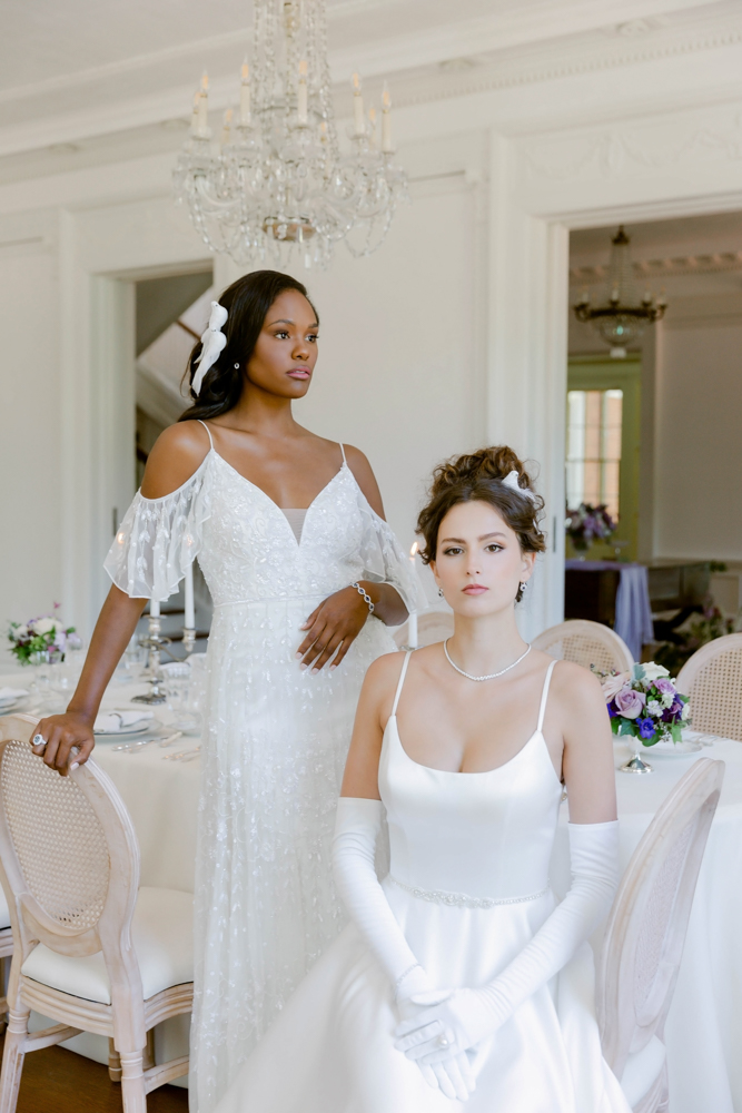 Two Alabama brides pose at the dinner table at The 1616 House in the wedding dresses from Bella's Bridal & Formal.