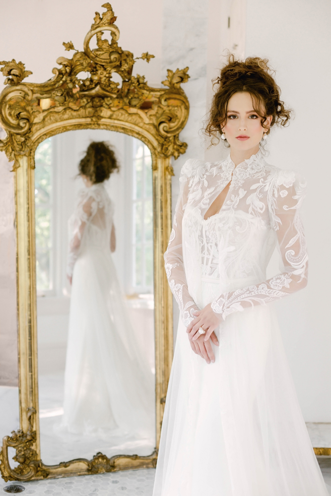 The bride wears her wedding dress from Bella Couture in front of an ornate mirror at The 1616 House in Montgomery, Alabama.