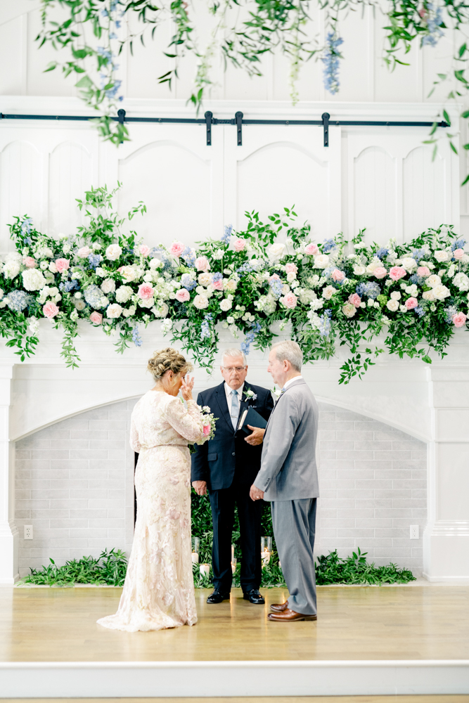 The couple renews their vows in front of a beautiful floral mantlepiece at Oak Meadow Event Center.