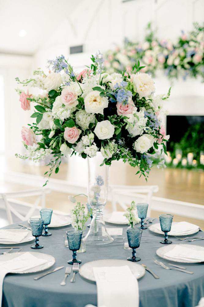 This blue, pink and white tablescape features a large floral centerpiece at Oak Meadow Event Center.