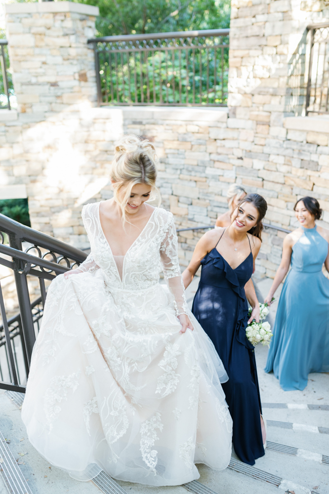 The bridal party in blue gowns escorts the bride up the stairs at Ross Bridge Golf Resort & Spa in Birmingham, Alabama.