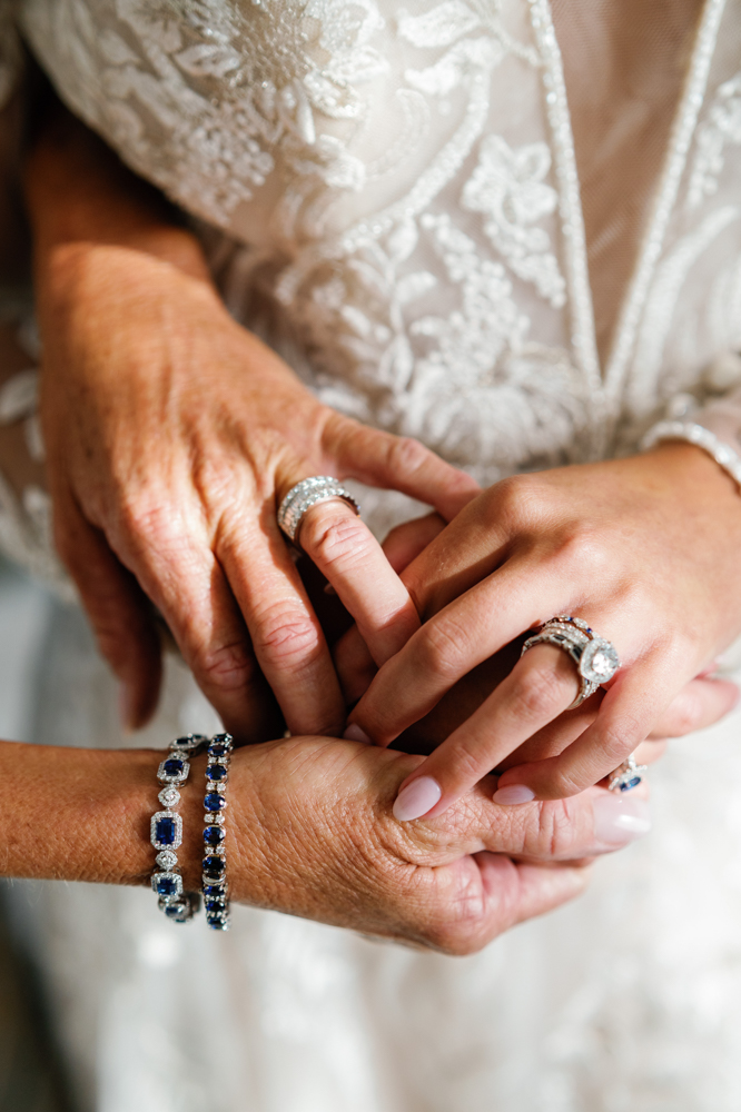 The bride and mother of the bride hold hands before the wedding, wearing blue gems from Bromberg's.