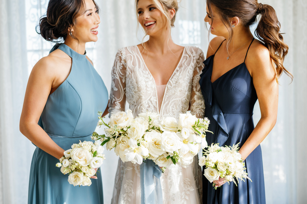 The bride and bridesmaids stand together with white floral bouquets by CeCe Designs.