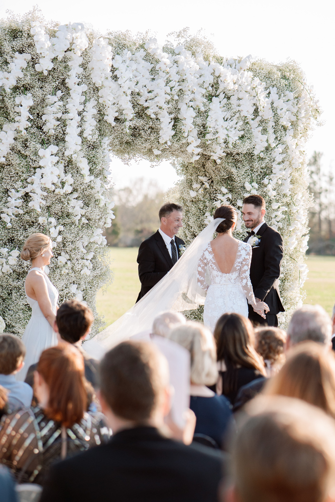 The bride and groom share their wedding vows surrounded by baby's breath and white orchids.