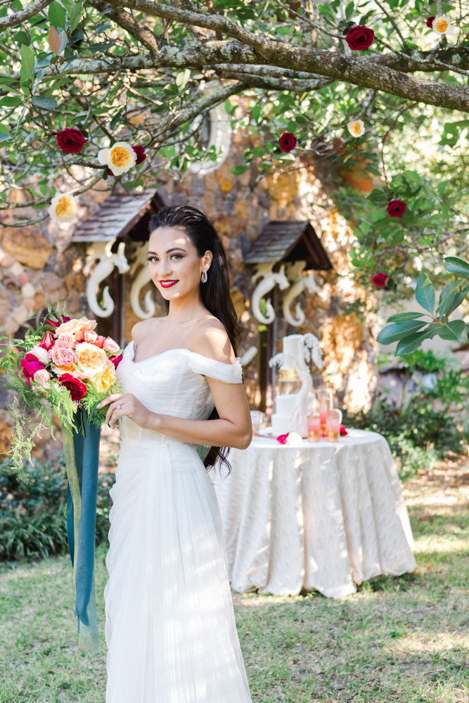 The bride poses in front of the wedding cake with her bouquet by Jubilee Flowers Fairhope in Alabama.