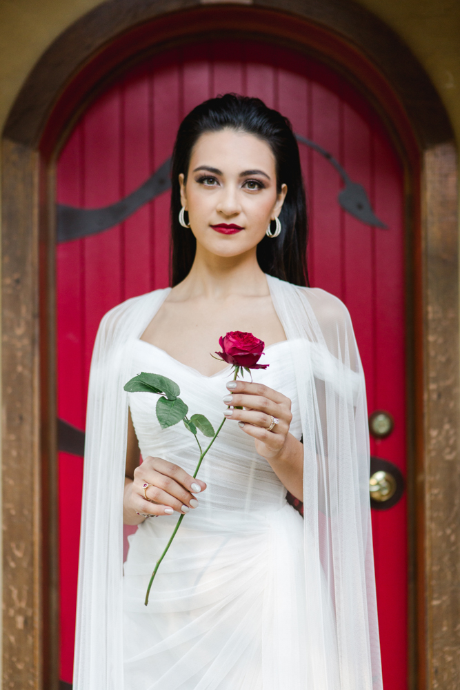 The Southern bride holds a rose in front of the red door.