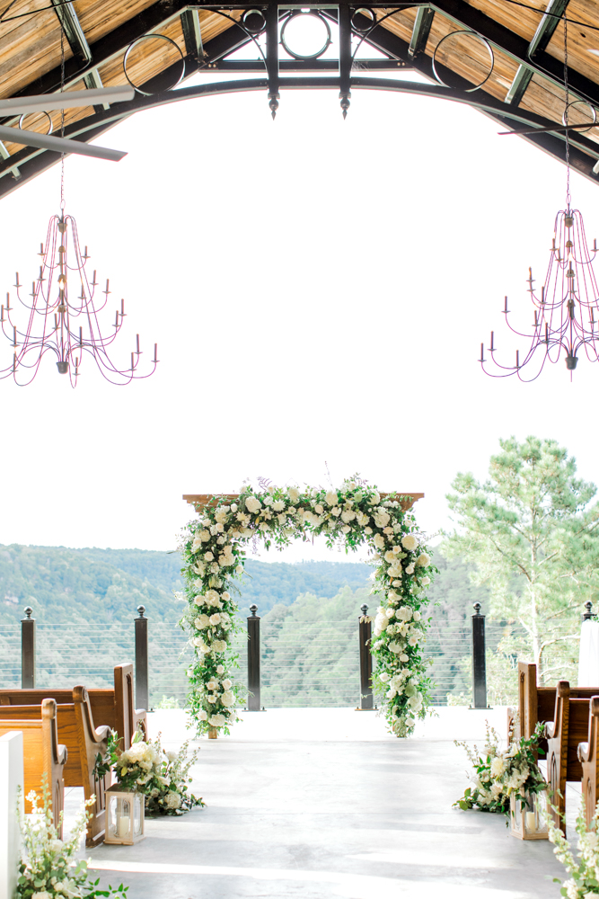 The Southern wedding ceremony at Burns Bluff at High Falls features a floral arch overlooking the view in Alabama.