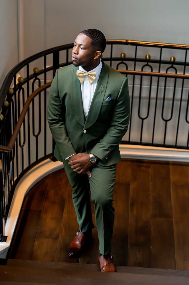 The groom poses in a green suit before a Birmingham wedding.