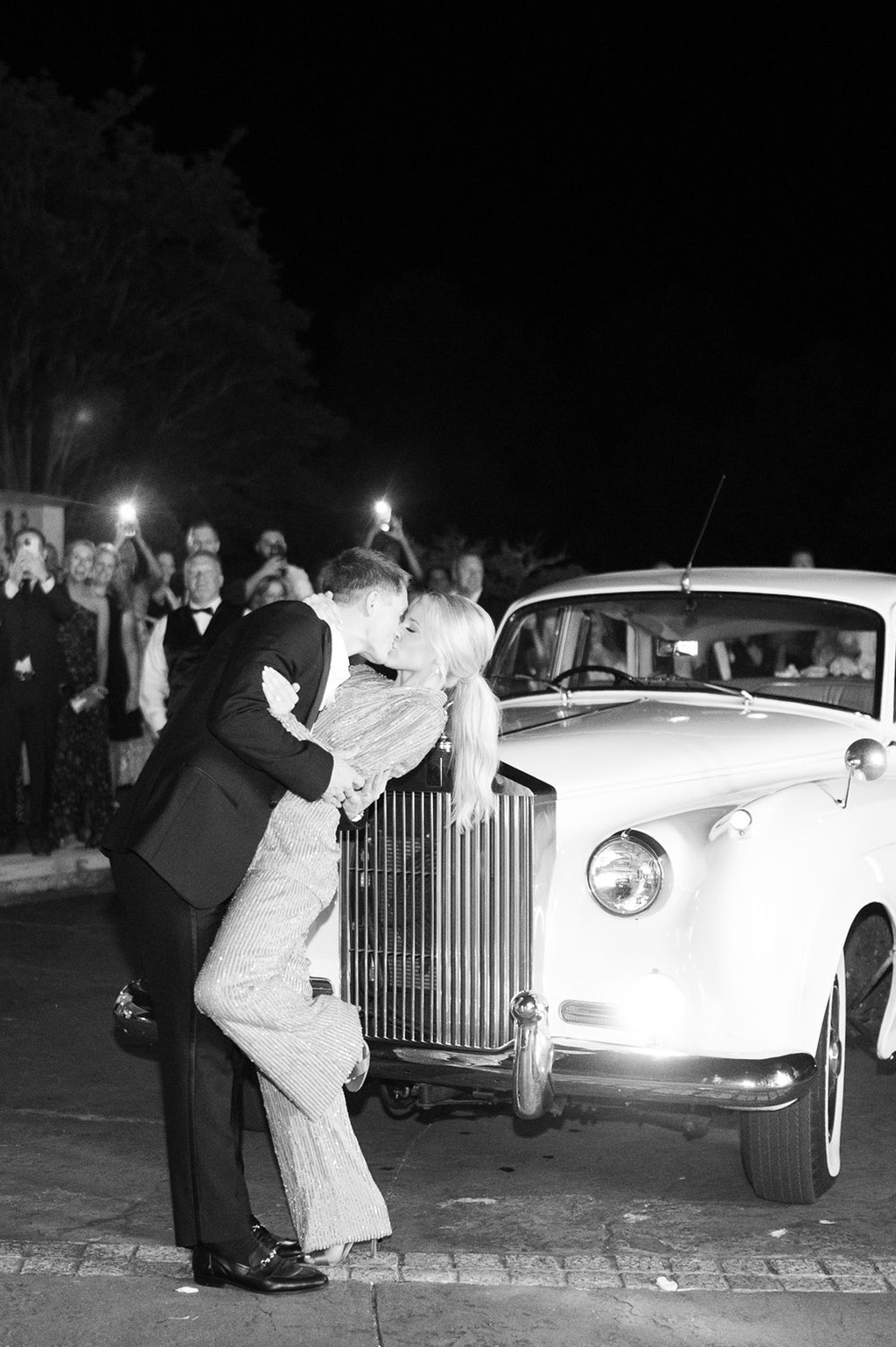 The bride and groom kiss in front of the getaway car from Coats Classic Cars.