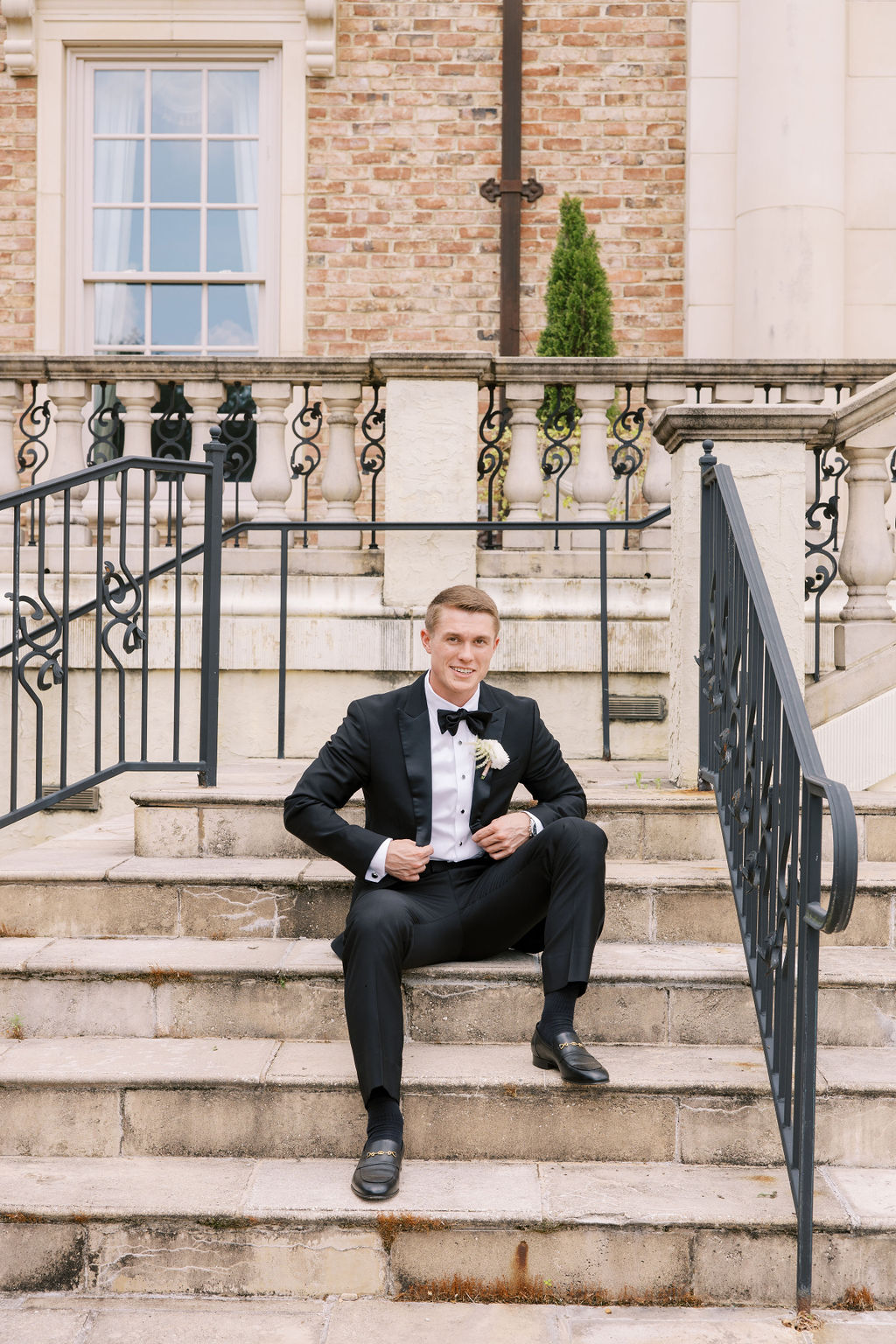 An Alabama groom wears a black tuxedo on the steps of Fountainview Mansion in Auburn.