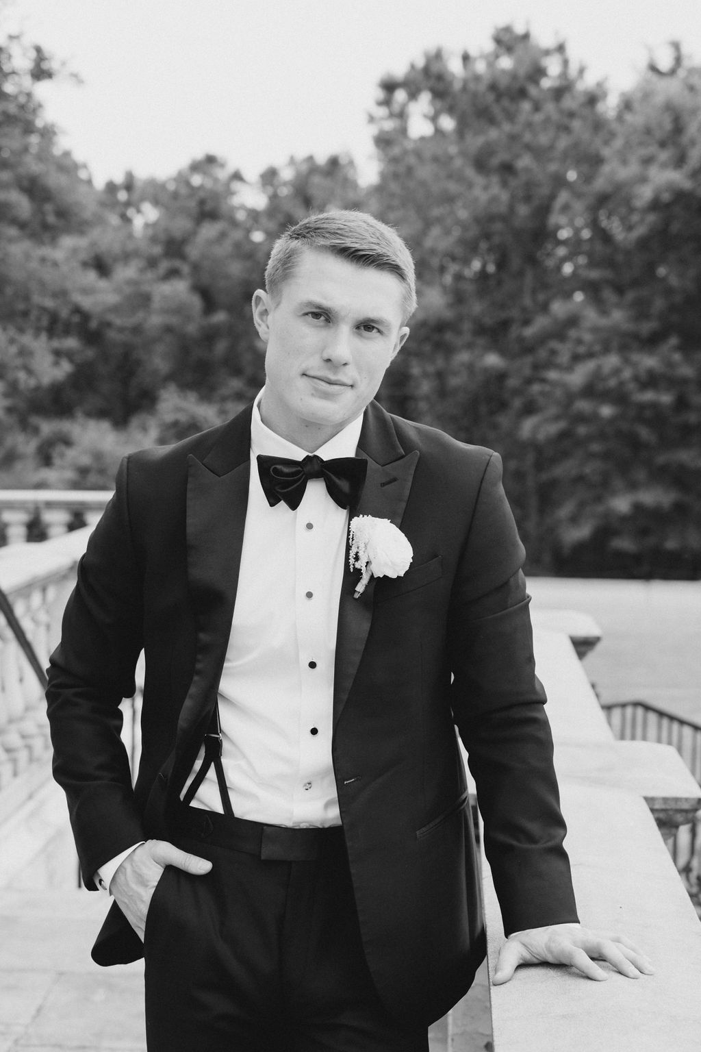 Alabama groom in tuxedo stands on the porch of Fountainview Mansion in Auburn.