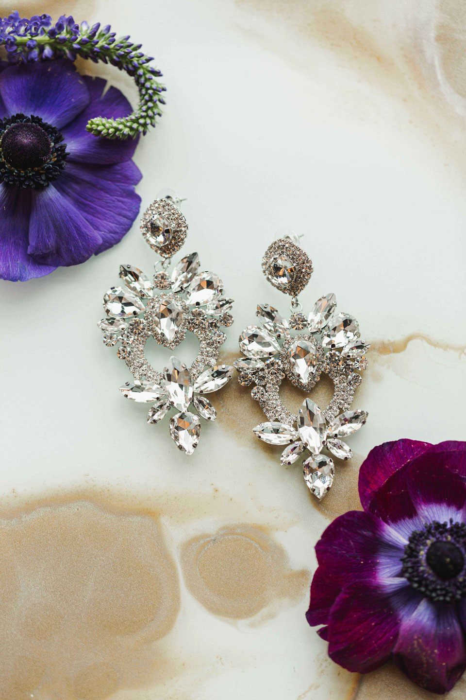 The earrings are photographed with purple flowers.