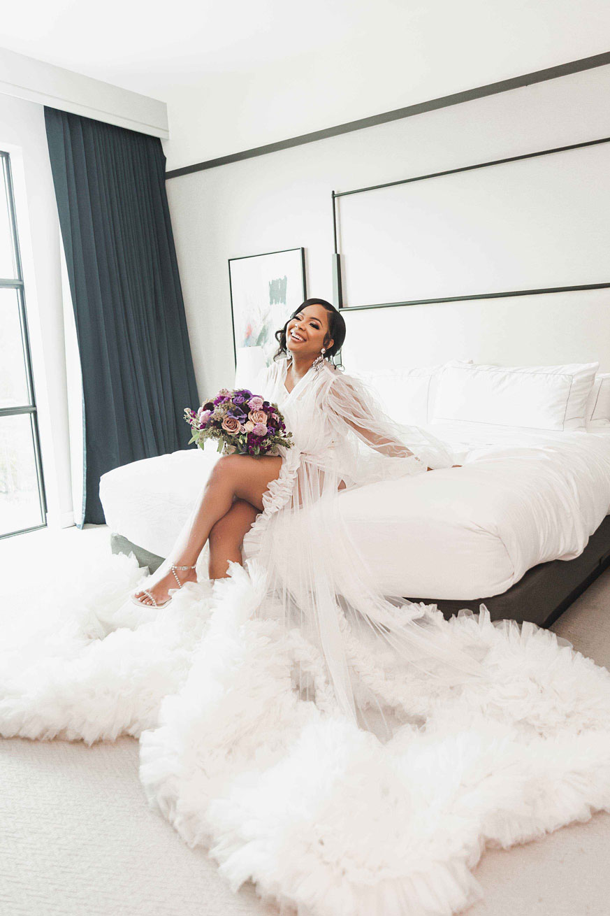 The bride sits on the bed with her bouquet before her Birmingham wedding day.