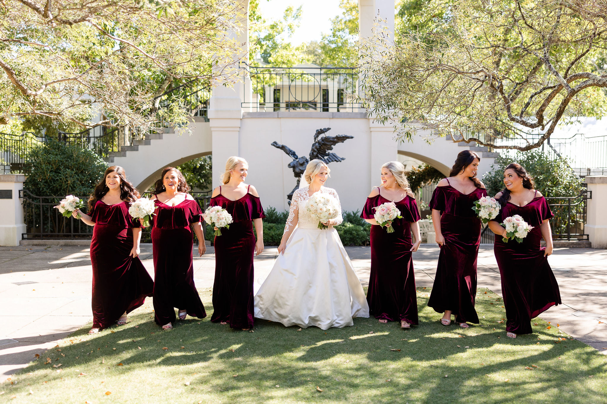 The bridesmaids wearing crimson velvet dresses walk with the bride at Birmingham Botanical Gardens.