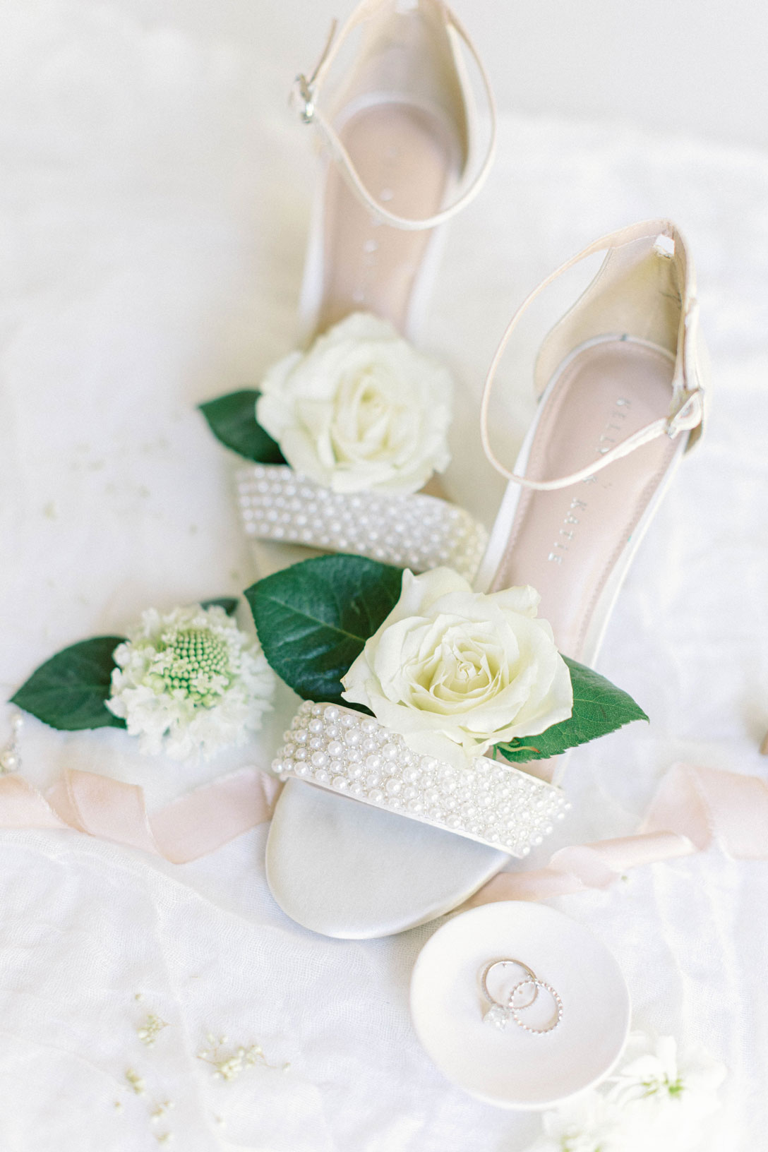 The bride's shoes are photographed with flowers and wedding rings.