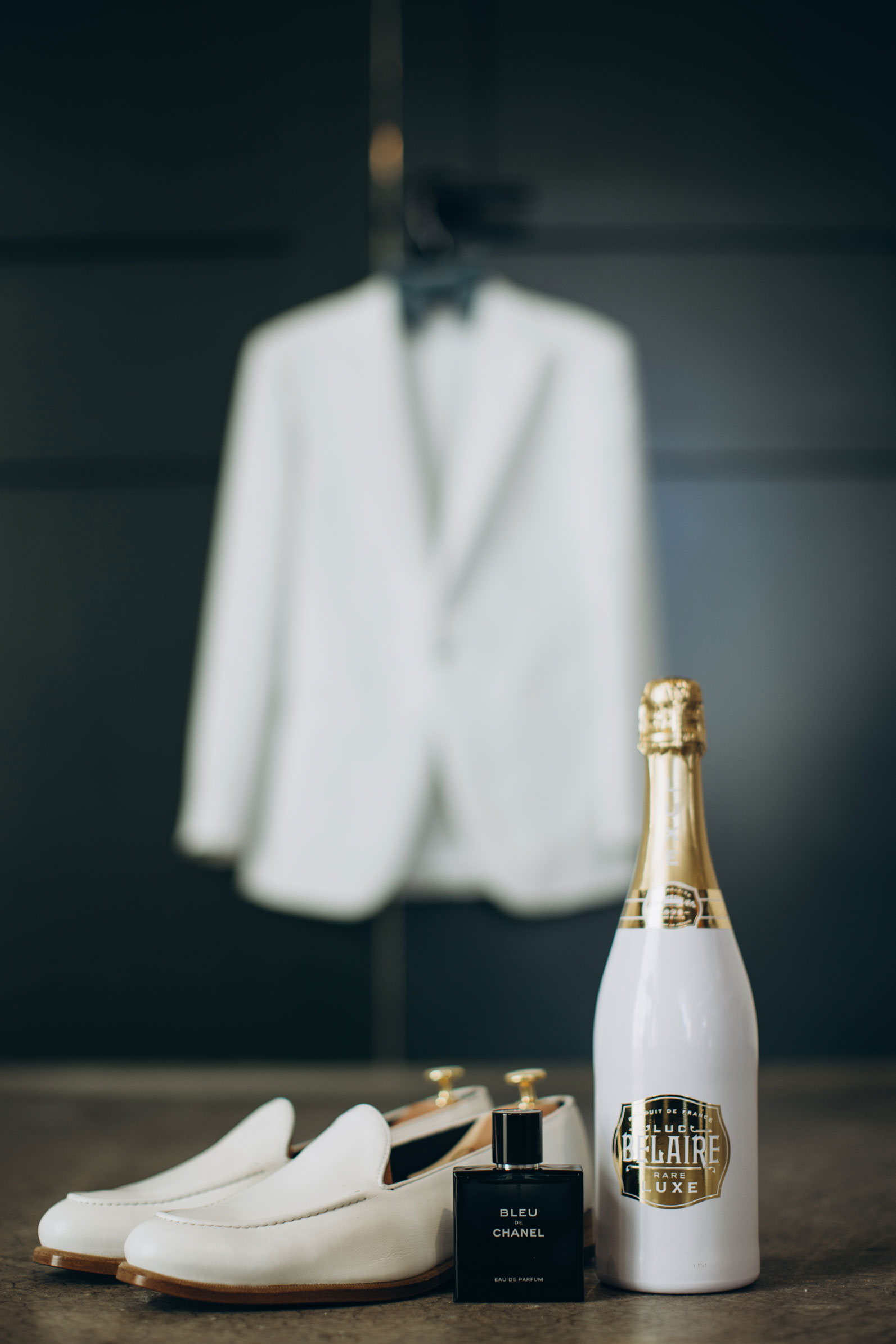 The groom's shoes and a bottle of champagne are styled in front of his white tuxedo.