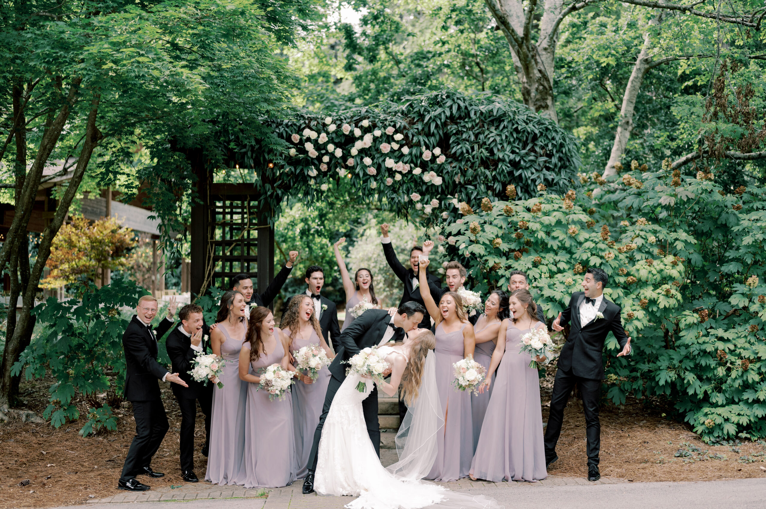 The wedding party cheers on the bride and groom as they kiss in the garden.