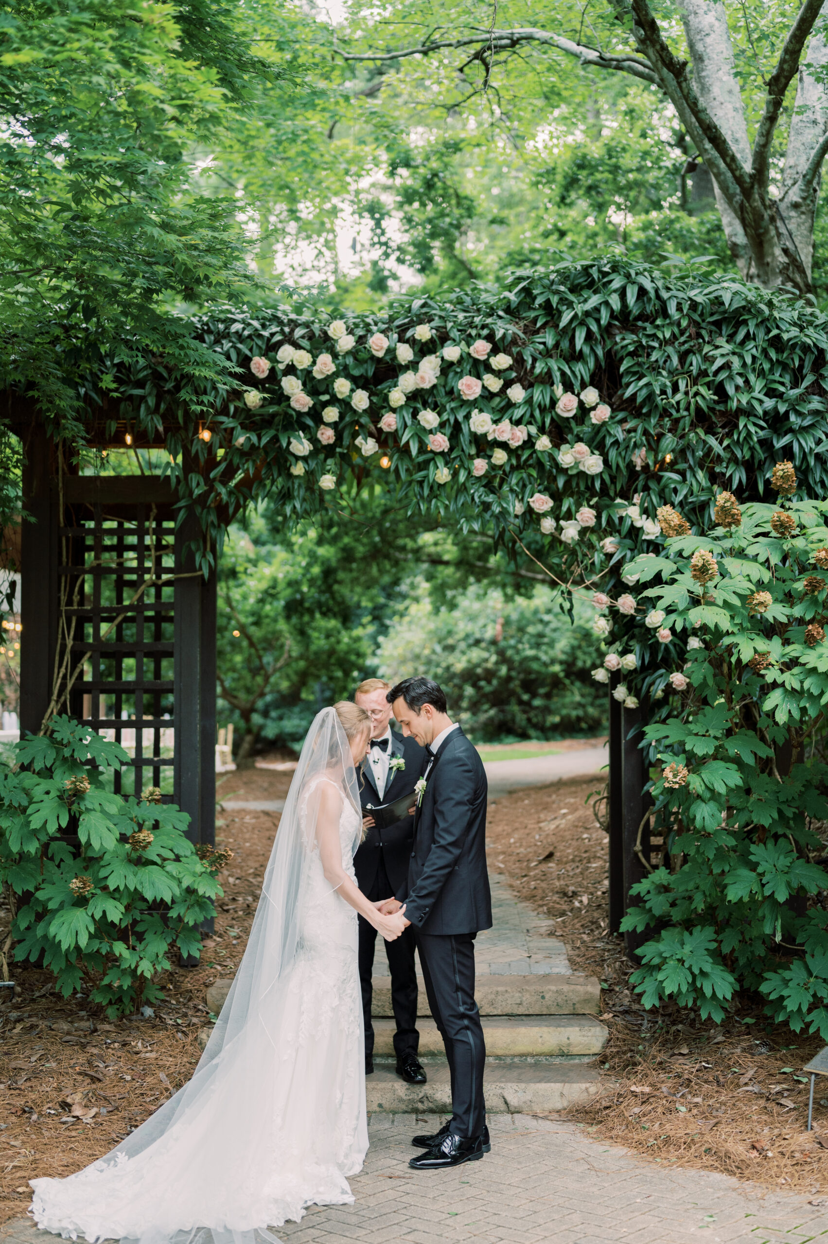 The bride and groom bow their heads together under the floral arch during their garden wedding.