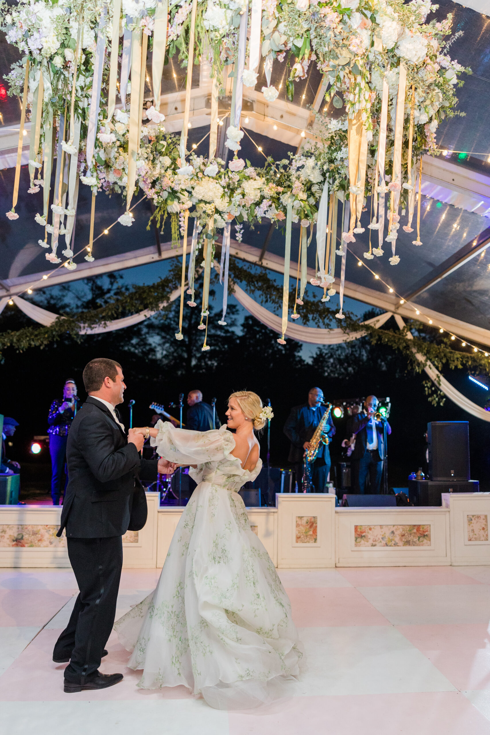 The bride and groom share their first dance under a floral chandelier in a clear top tent in Alabama.