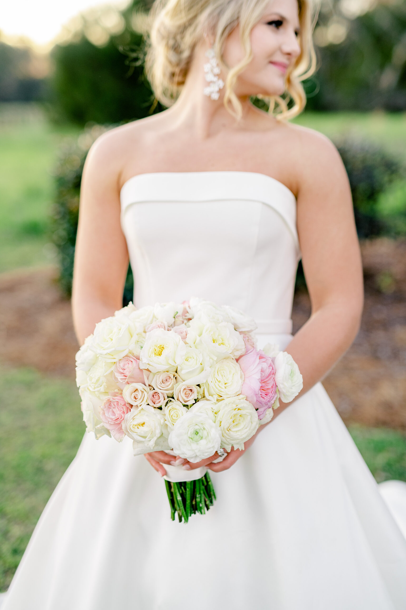 The bride displays her bouquet with roses and pink flowers.