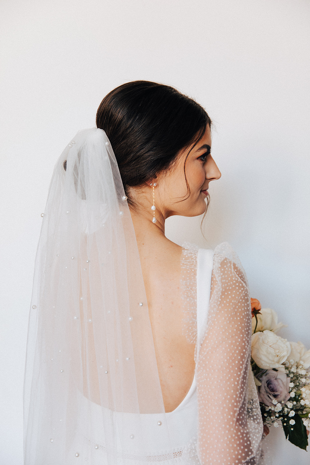 The bride shows her drop pearl earrings that match her pearled veil from Birch on Main in Huntsville, Alabama.