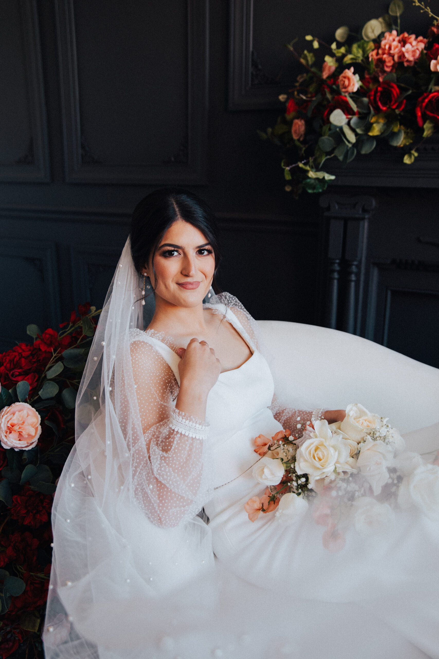 The bridal portraits are taken against a black wall while she sits on a chaise.