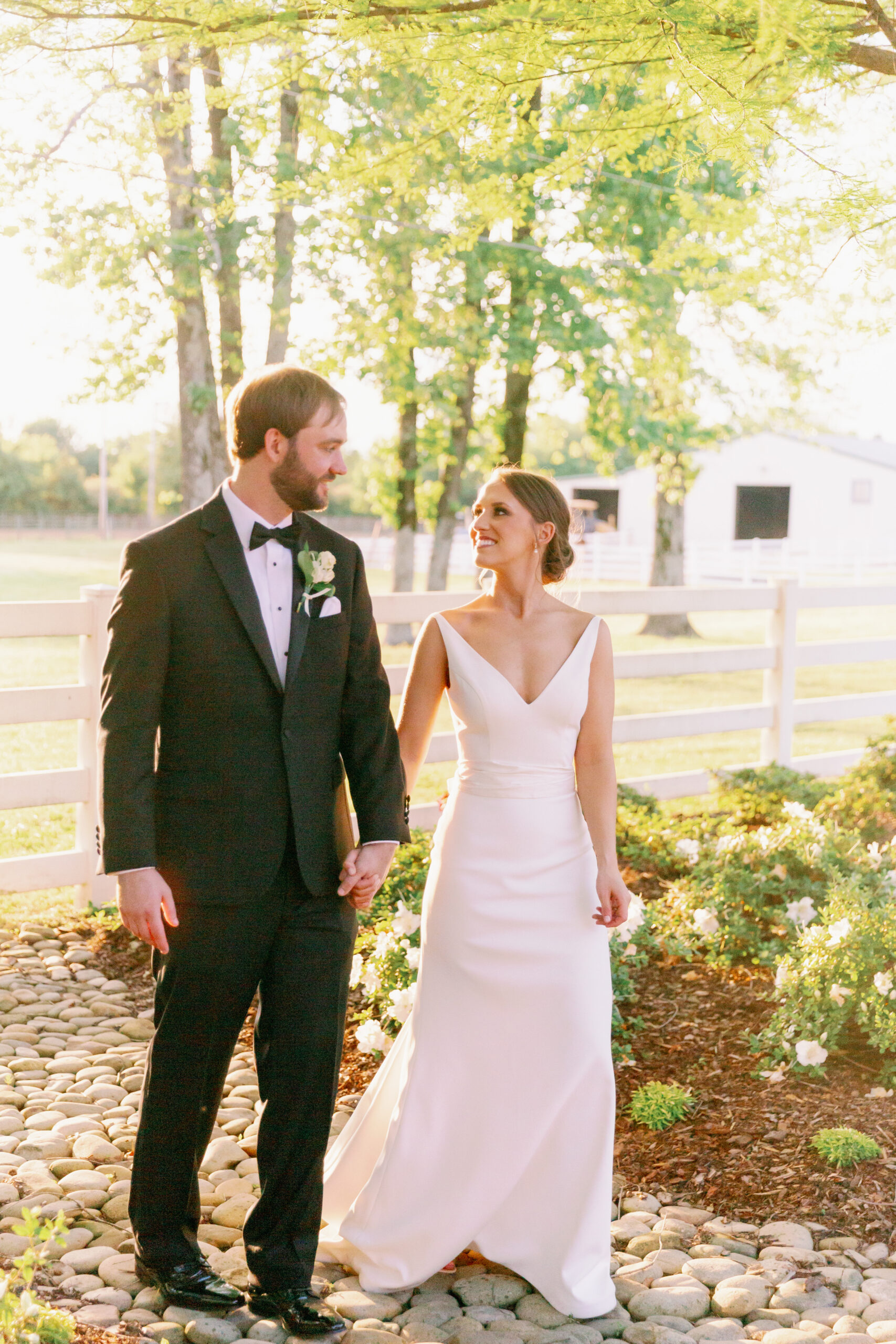 The bride and groom walk together by a white fence in Alabama.