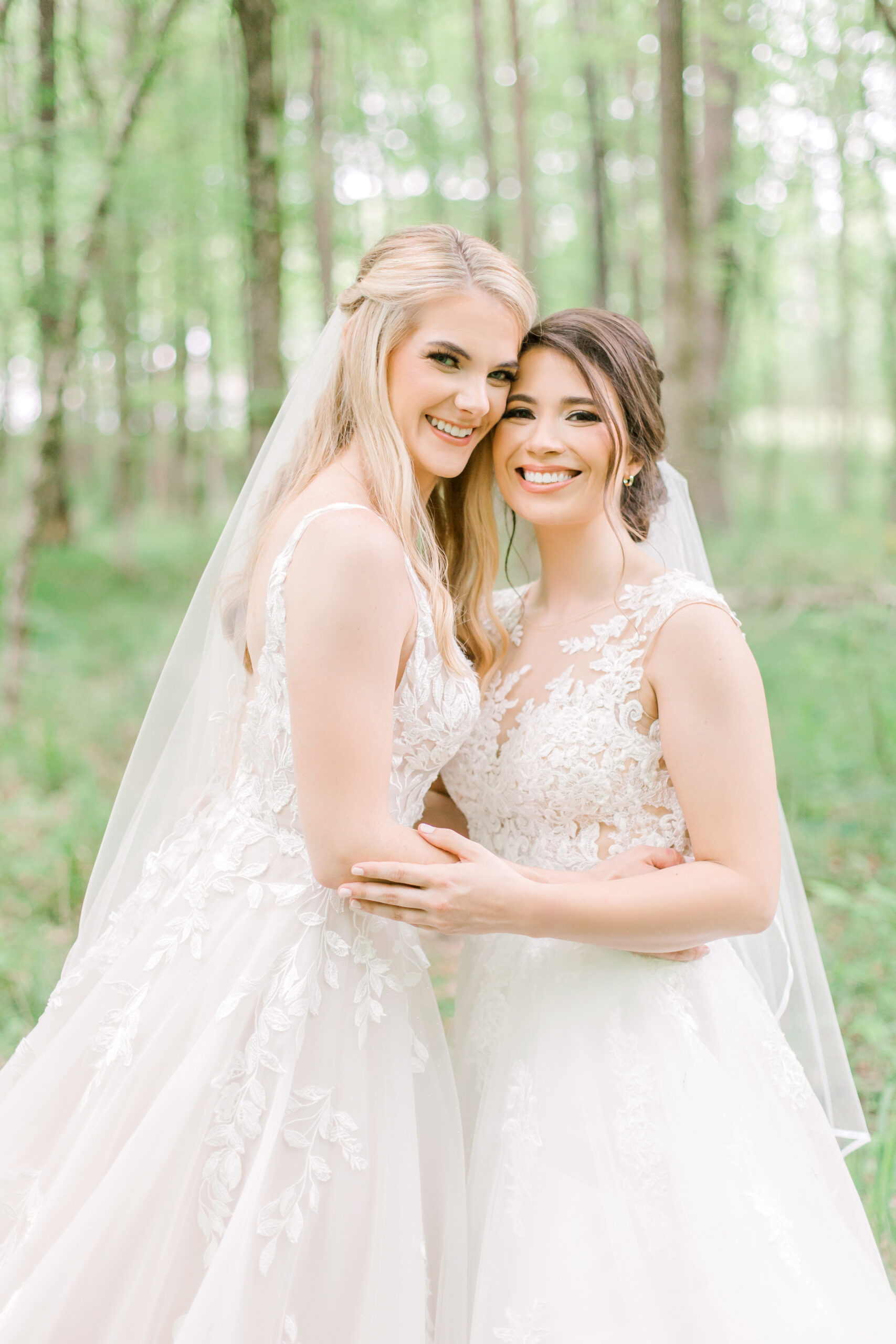 The brides embrace in their wedding dresses in the woods