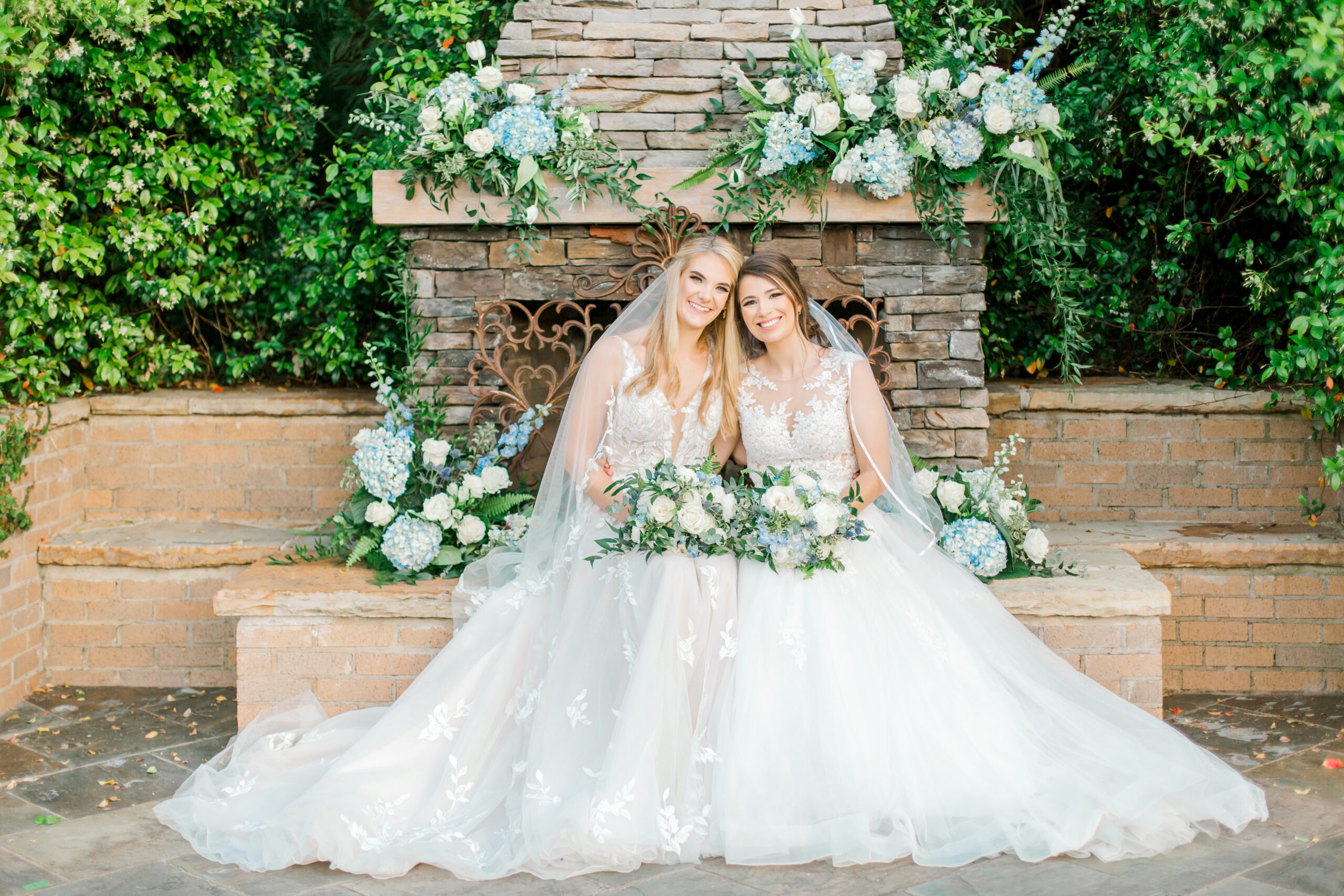 The brides pose together in front of the outdoor fireplace.