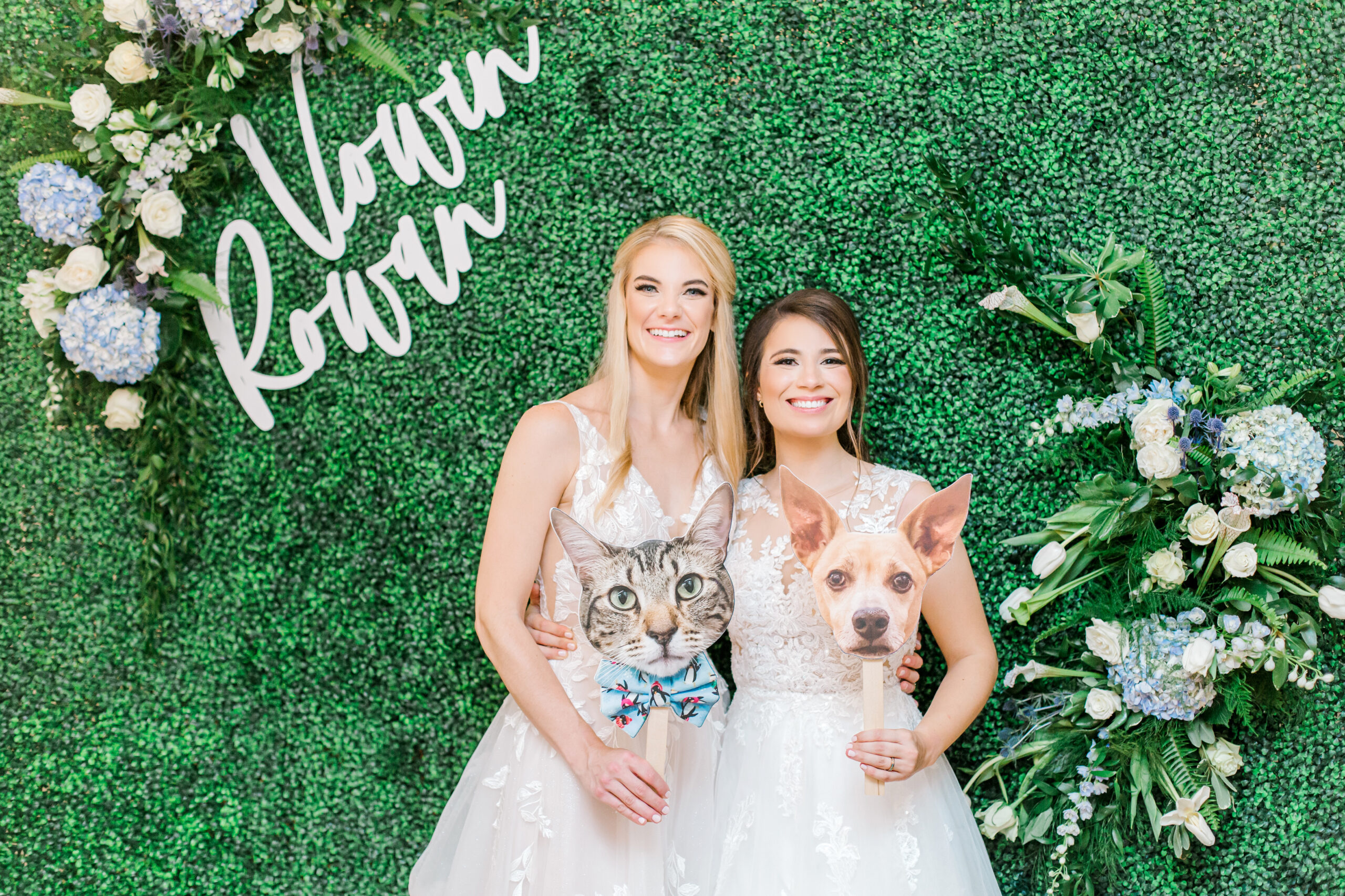 The brides pose together in front of a boxwood wall during the Southern wedding reception.