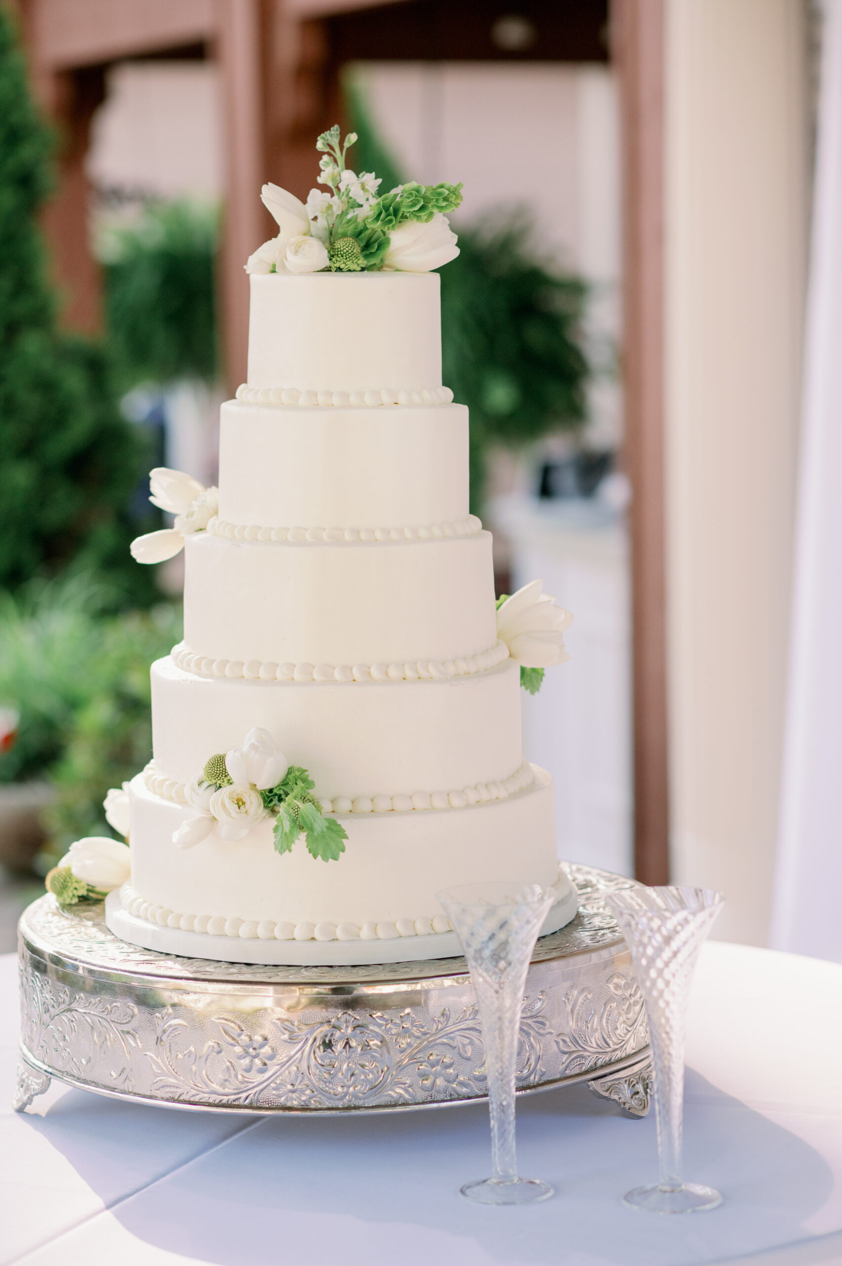 The classic wedding cake is on a silver cake stand with champagne flutes.