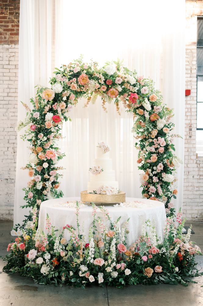 The wedding cake from Olexa's Cafe is under an arbor of fresh flowers for the Southern reception.