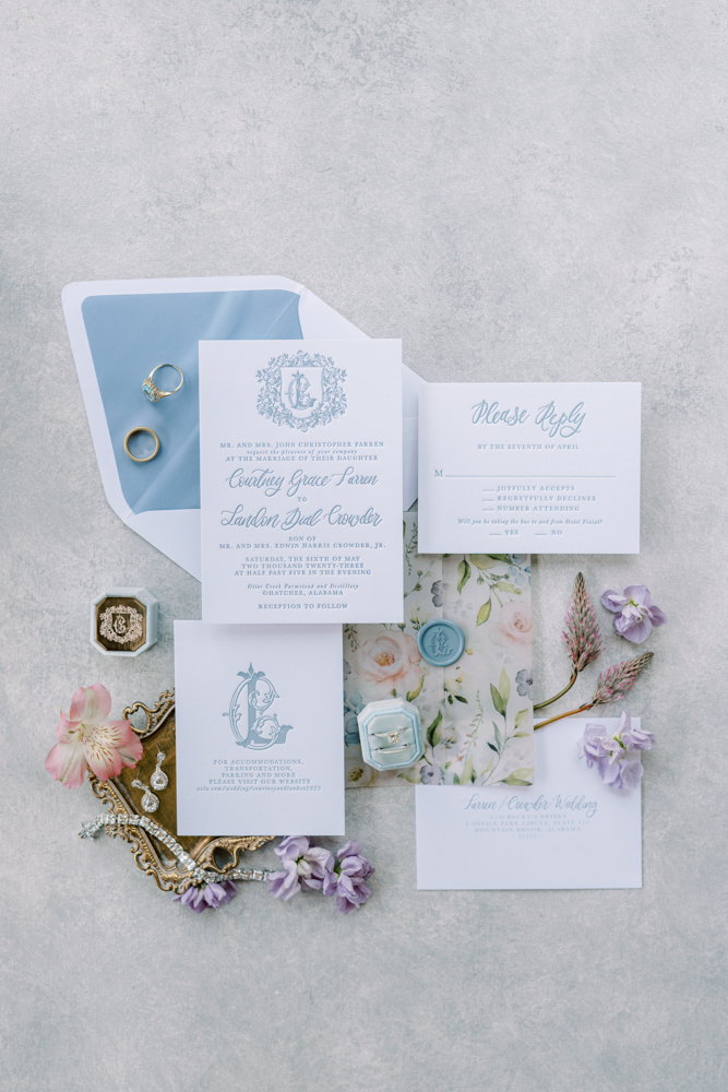 The blue wedding invitations are styled in a lay flat with the bride's jewelry.