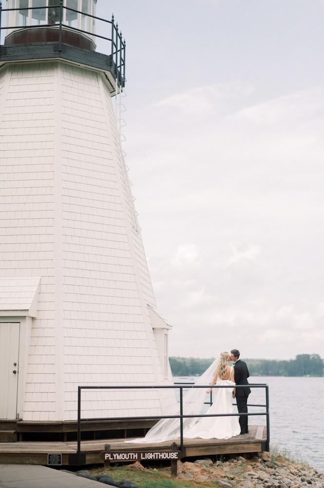 The bride and groom kiss beside the lighthouse at Children's Harbor in Alabama.