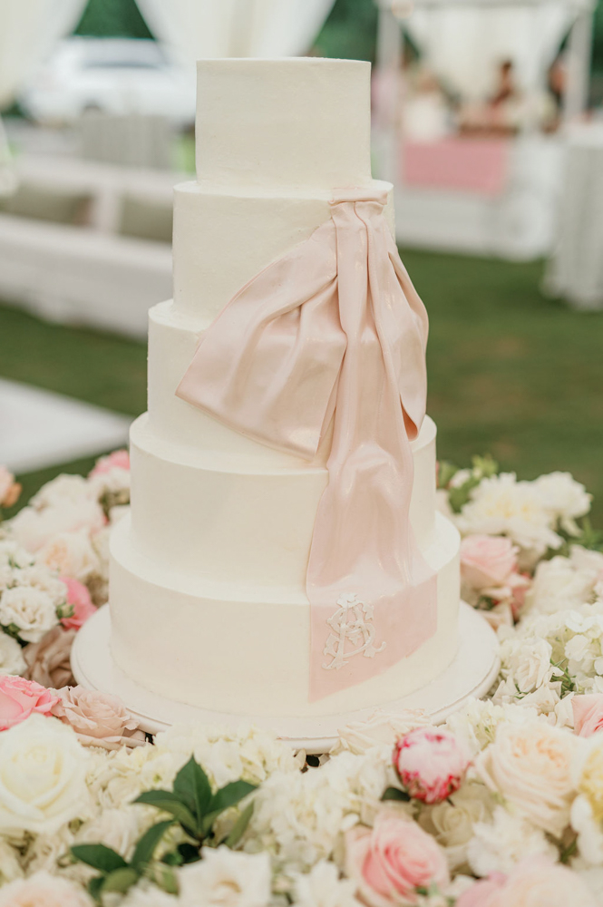 The wedding cake is decorated with a sugar ribbon on a bed of flowers for a Southern wedding reception.