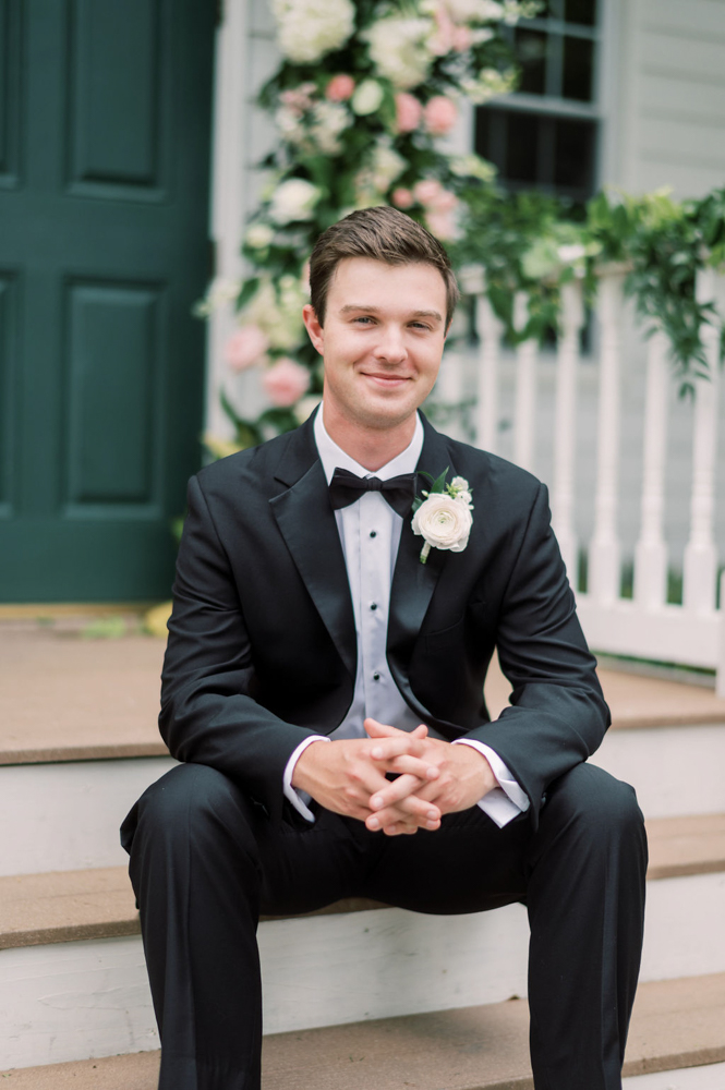 The groom sits in his tuxedo on the steps of the chapel at Children's Harbor in Alabama.